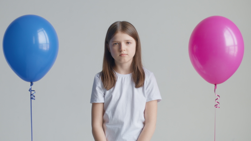 A teen girl in a white T-shirt stands between blue and pink balloons and cannot make a choice Royalty-Free Stock Footage #1087462709