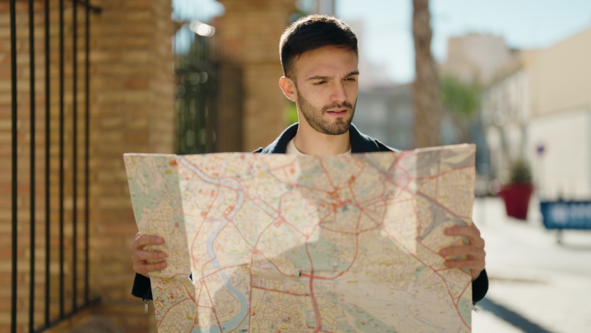 Young hispanic man looking city map at street