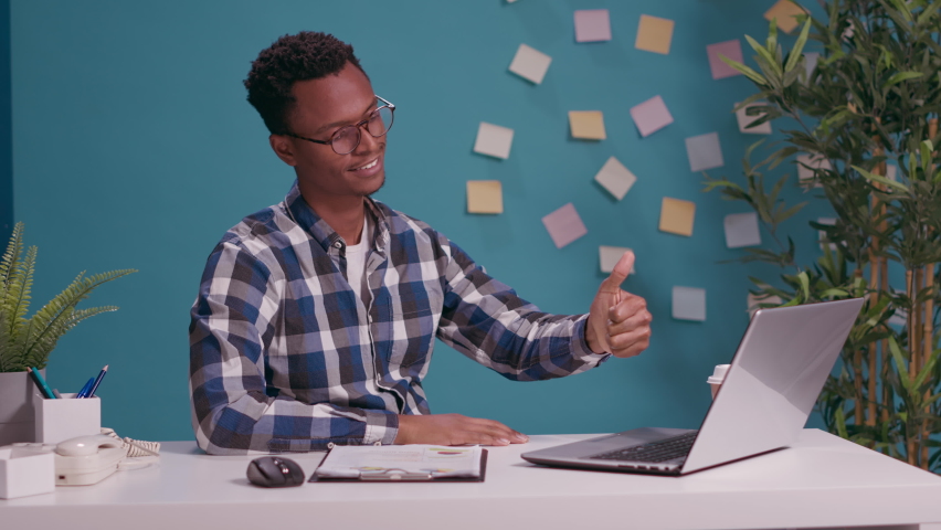 Positive adult doing thumbs up and okay gesture with hands, confirming success in front of laptop screen. Cheerful man showing approval and accept symbol with fingers, confident agreement.