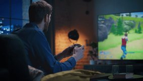Young Man Spending Time at Home, Sitting on a Couch in Stylish Loft Apartment and Playing Arcade Shooter Video Game on Console. Male Using Controller to Play MMO Battle Royale Style Game Online.