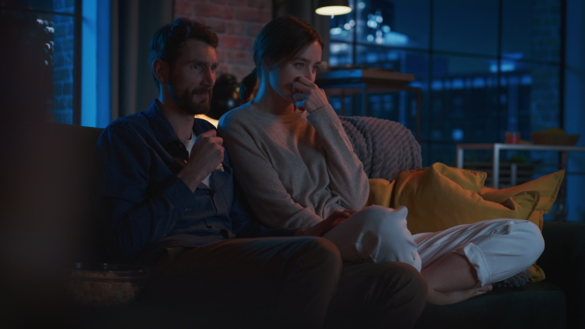 Portrait of Beautiful Couple Spending Time at Home, Sitting on a Couch, Watching Scary TV Show in Their Stylish Loft Apartment. Man Puts Hand on Female Knee, While Streaming Thriller Movie. | Shutterstock HD Video #1087466315