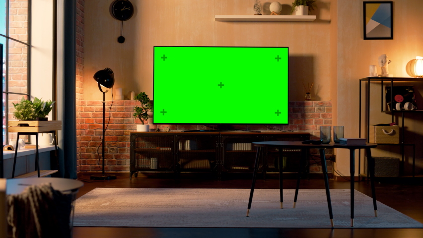 Stylish Loft Apartment Interior with TV Set with Green Screen Mock Up Display Standing on Television Stand. Empty Living Room at Home with Chroma Key Placeholder on Monitor. Zoom Out Sunset Warm Shot. | Shutterstock HD Video #1087466408