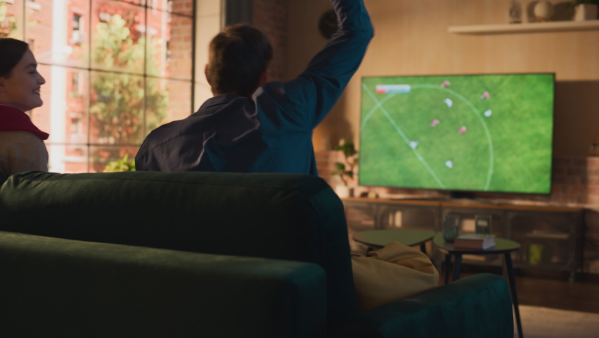 Couple of Soccer Fans Relax on a Sofa, Watch a Sports Match at Home in Stylish Loft Apartment. Excited Young Man and Woman Cheer for Their Favorite Football Club, Celebrate Player Scoring a Goal. | Shutterstock HD Video #1087466447