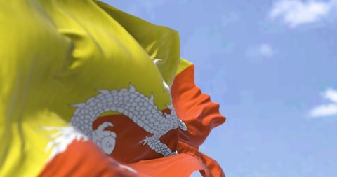 Detail of the national flag of Bhutan waving in the wind on a clear day. Bhutan is a landlocked country in the Eastern Himalayas. Selective focus. Seamless looping in slow motion