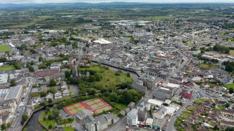 Forwards fly high above town. Sport centre and historic town borough on river bank. Aerial panoramic shot. Ennis, Ireland