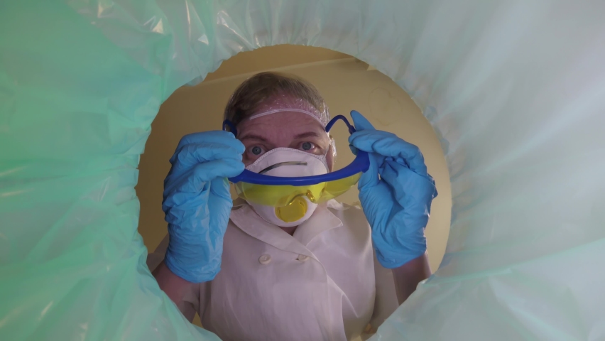 Woman doctor in medical respirator with hight protection throwing used medical trash in bin away, trash bin with pills, medical mask, galsses inside, medecine in trashcan