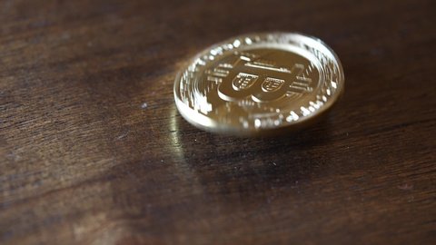 Gold Bitcoin wobbling on a wooden tabletop. Slowed to quarter speed.