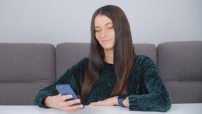 Beautiful Caucasian woman wearing green sweater and modern smart watches using mobile phone. White female browsing internet news feed on cellphone. Millenial person communicating online on social app