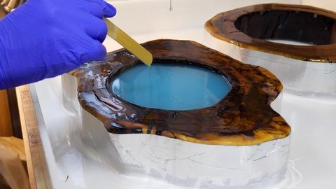Process making of a craft resin and wood table. Liquid epoxy is poured into a mold with wooden blanks.