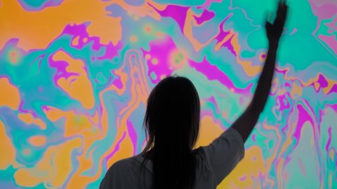 NIZHNY NOVGOROD, RUSSIA - AUGUST 28, 2021: Augmented reality event - back view: woman waving arms and moving in front of colorful large wall display with mirror effect at AR immersive exhibition: redactionele stockvideo