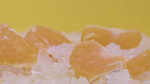 A slice of tangerine falls on the table near tangerines with green leaves on a yellow background. Filmed on high speed cinema camera, 4K.