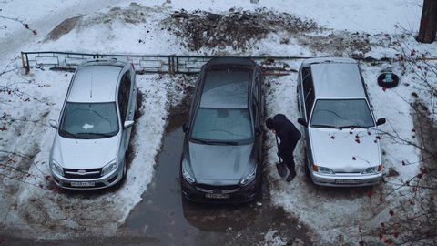 A man removes snow in winter under a place for a car in the rain