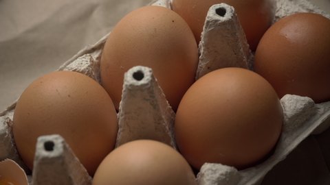 The broken egg lies in the container among the whole eggs. Chicken yolk. Chicken brown fresh raw eggs in a paper box. An egg carton with ten eggs. Lots of fresh raw chicken eggs. Omelette. 4k
