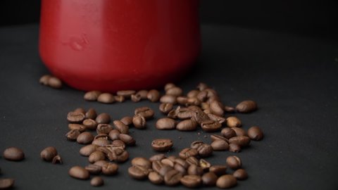 Coffee beans are hung out of the Red cezve in Slow Mo. Slowly scattered coffee on a black surface. Coffee house. Fried aromatic coffee.