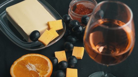 The girl takes grapes against the background of a glass of wine and snacks. Aesthetics of wine with cheese. Alcohol, romance, evening. Cheese, butter, red caviar, grapes, baguette, orange. View from