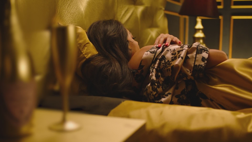 Beautiful Young Woman Sleeping Dreaming and Flirting in Bed . Female model resting laying asleep inside luxury golden bedroom . Golden room in hotel , house . Shot on ARRI cinema camera in slow motion