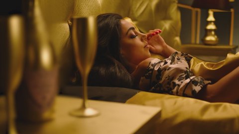 Beautiful Young Woman Sleeping Dreaming and Flirting in Bed . Female model resting laying asleep inside luxury golden bedroom . Golden room in hotel , house . Shot on ARRI cinema camera in slow motion