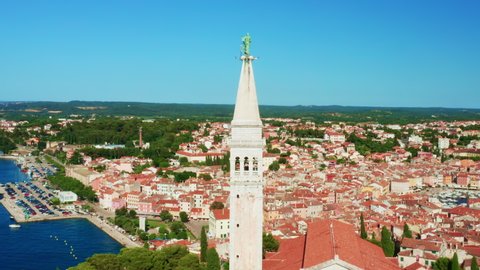 Church of St. Euphemia tower in Rovinj and surroundings. Old Croatian town buildings with red rooftops surrounded by forests and Adriatic sea. Aerial panorama