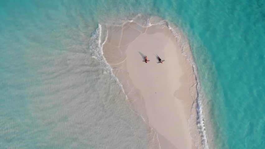 Drone aerial view of caucasian couple laying on sandbank with arms spread out between turquoise water, white sand and little waves, Dharavandhoo, Maldives, Indian Ocean. Royalty-Free Stock Footage #1087485803