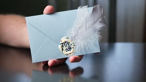 Envelope sealed with sealing wax and decorated with a feather in a man's hand. Correspondence, love letter concept.
