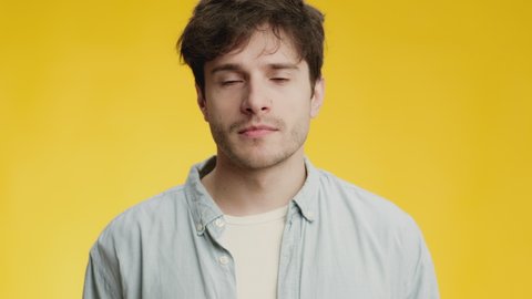 Disgusting air smell. Close up portrait of young man feeling awful aroma, frowning face and feeling gagging sensation, yellow studio background, slow motion