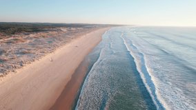 Drone following the coastline along a sandy beach with rolling ocean waves.