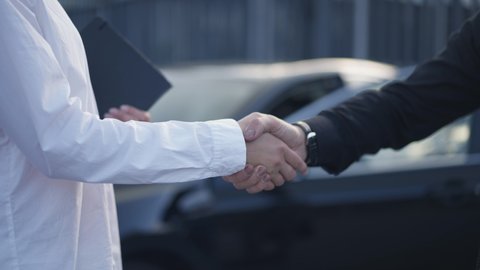 Handshake of Caucasian man and woman on city street in front of black car. Unrecognizable business partners shaking hands in slow motion leaving. Cooperation and partnership concept