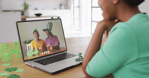 Smiling african american male friends with beer wearing clover shape items on video call on laptop. irish tradition and st patrick's day celebration concept digitally generated video.
