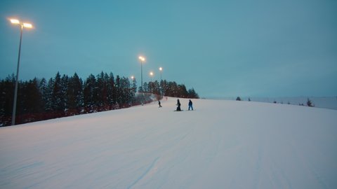 People go downhill on the slope of the skiing center at sunset