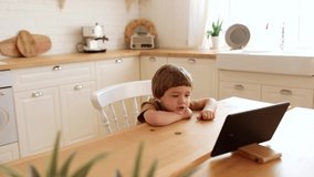 a little caucasian boy eats krunchy breakfast and watches tablet PC at kitchen 