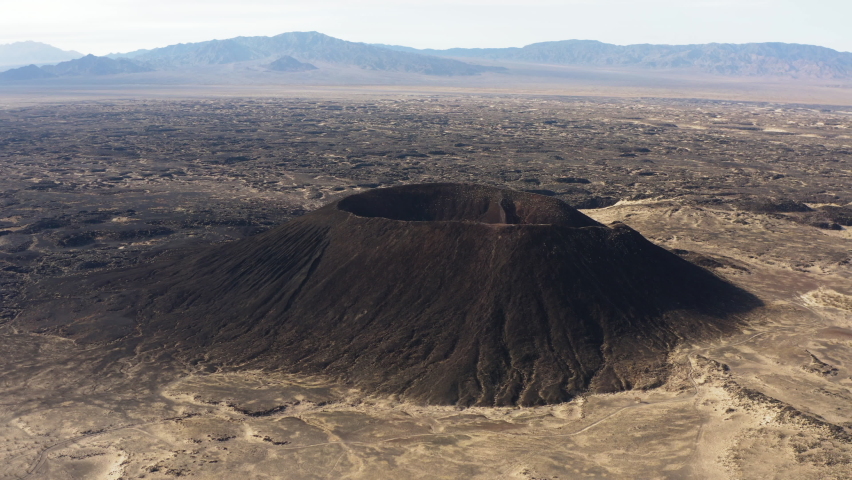 Aerial landscape view of Amboy Crater dormant cinder cone volcano that rises above lava field rock bound formation in the eastern Mojave Desert of southern California