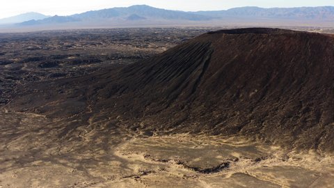drone close up of Amboy Crater dormant cinder cone volcano rises above lava field geologic rock formation in the eastern Mojave Desert of southern California during a sunny day