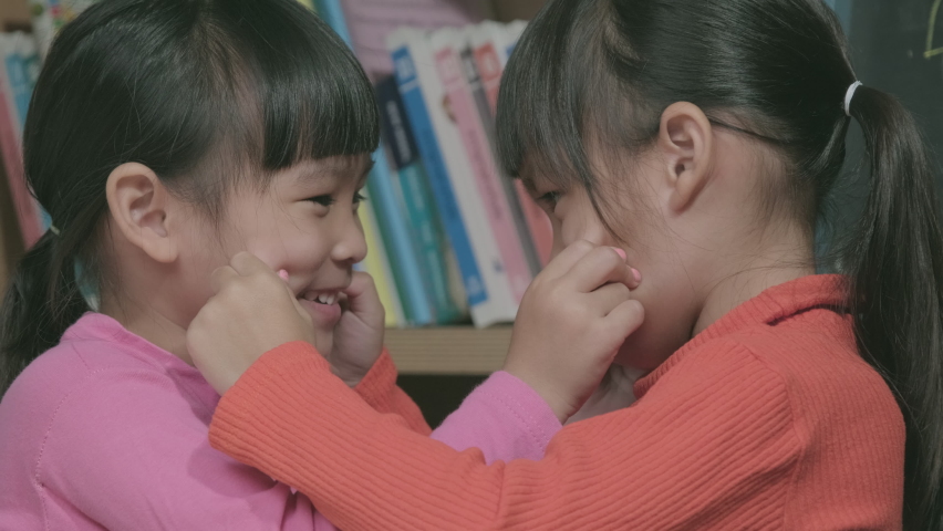 Asian sisters touch each other's cheeks and smile face to face. two cute little girls playing together at home. Lovey family spending time together indoors.
