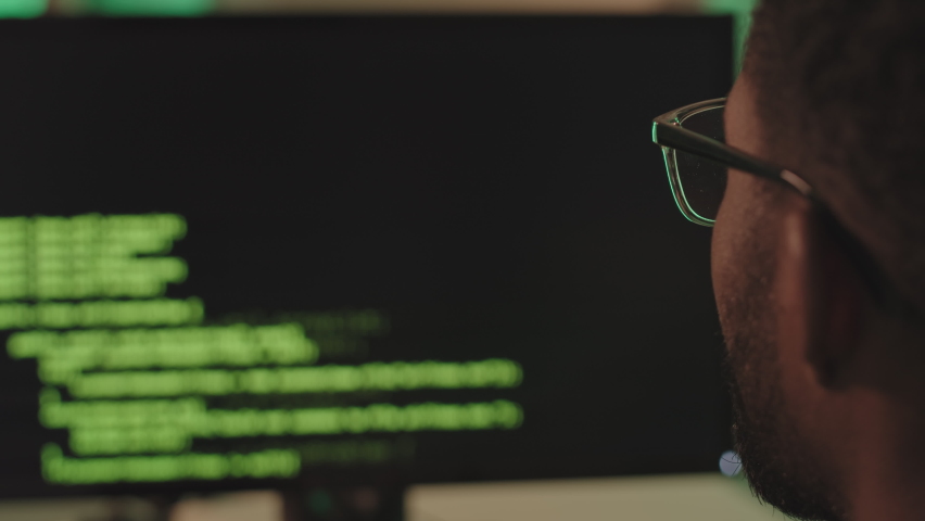 Close-up of African-American programmer looking at black computer screen with running program code