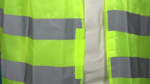 Close-up view 4k stock video footage of adult white man putting on bright yellow reflective vest or safety jacket