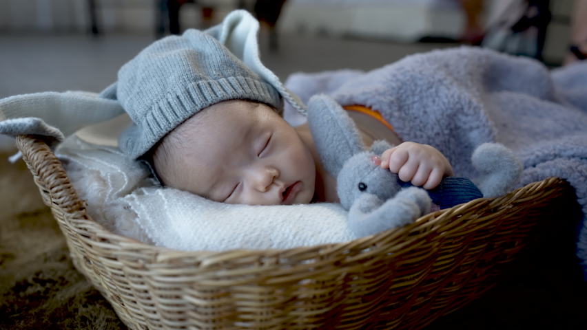4k, Cute Asian newborn baby. wearing a blue rabbit Sleep well. By hugging the rabbit doll. lying in a wicker basket	