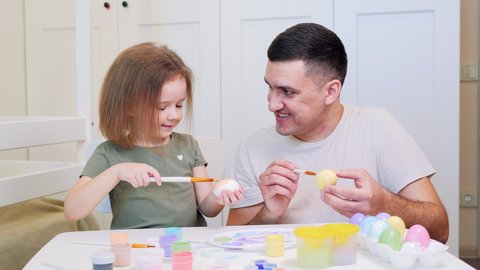 Happy easter. Little daughter and dad painted eggs at home. Daughter kisses Dad on cheek. A daughter's love for her father. A young handsome man with a funny little child is painting eggs