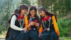 Three cheerful Asian Indian females or rural girls use mobile phone to watch a movie or video on an OTT platform or social media together in a remote or a village area. Concept of online entertainment