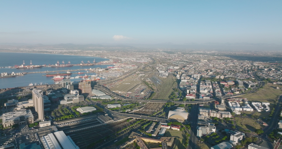 Aerial panoramic shot of transport infrastructure in large city. View of big oversea harbour, train station with extensive rail tracks and busy trunk roads. Cape Town, South Africa