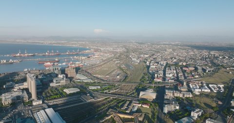 Aerial panoramic shot of transport infrastructure in large city. View of big oversea harbour, train station with extensive rail tracks and busy trunk roads. Cape Town, South Africa