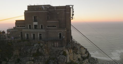 Building on upper cable car station on famous Table Mountain. High rock wall steeply falling to valley. Slide and pan shot in sunset time. Cape Town, South Africa