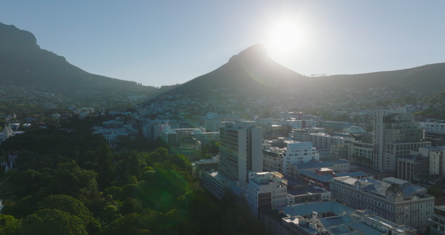 Town development and Lions Head mountain against bright sun. Forwards fly above buildings in City Bowl. Cape Town, South Africa