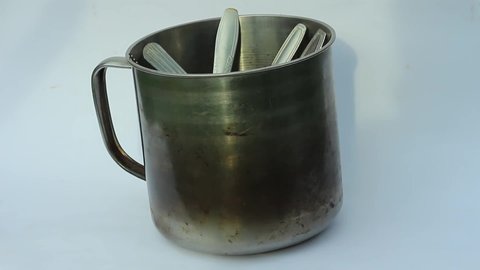 The stainless steel drinking cup is large and has one handle. Kitchen utensils close-up isolated on a white background. In the cup there is a tablespoon