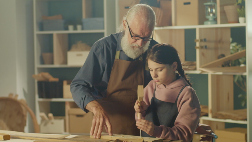 Grandfather Carpenter with Granddaughter Work with Wood to Create Items or Furniture Using Carpentry Tools. Training in Craft Skills in Home Workshop. Communication of Generations. Handicraft, Hobby. Royalty-Free Stock Footage #1087529696