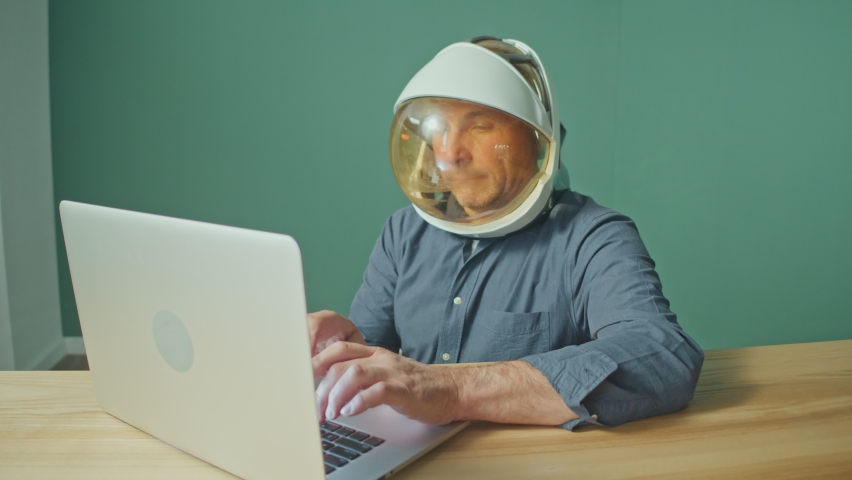 A Strange Man in a Space Helmet From a Spacesuit in a Cheerful Mood Works on a Laptop at the Table. Espionage, 5G Waves Destroying the Brain, Mind Control and People Control. Isolation, Mental Health. Royalty-Free Stock Footage #1087529732