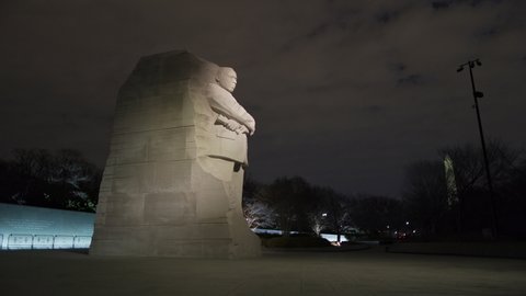 Washington, DC - USA - February 16 2022: The Martin Luther King Jr. Memorial statue in seen at night in the winter. The Washington Monument is seen in the background through the trees.