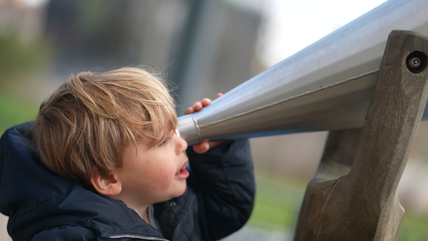 Toddler boy looking through large binocular shape object outdoors
