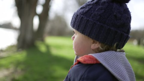 Contemplative Cute baby toddler child wearing beanie during winter season standing outside at park