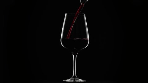 red wine being poured into a glass on a black background with rim lighting, slow motion