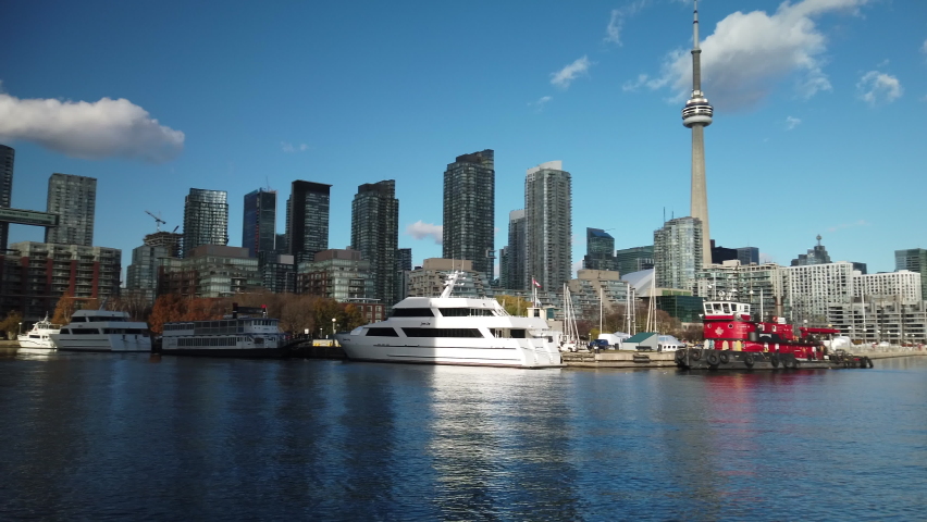 Wide establishing shot of boats moored in Toronto harbour with city skyline in the background